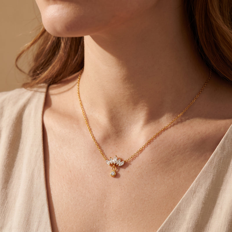 Close-up view of a model wearing the gold-tone lotus marquise drop necklace on a cream V-neck top.