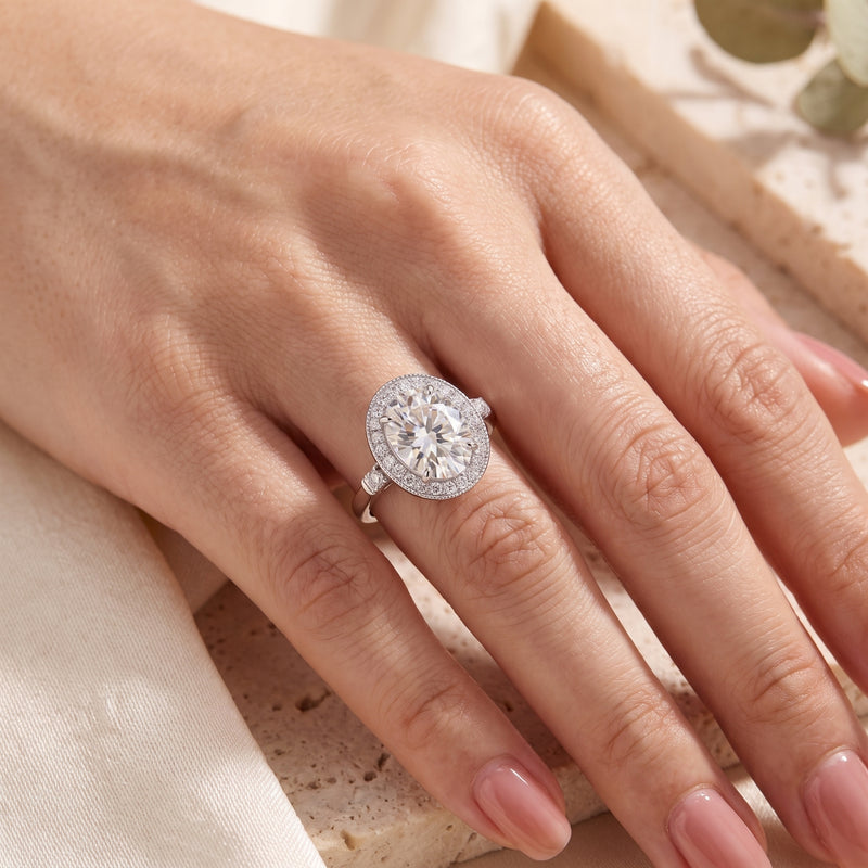 Close-up of a hand wearing the silver oval halo ring, showing its center stone and detailed halo.