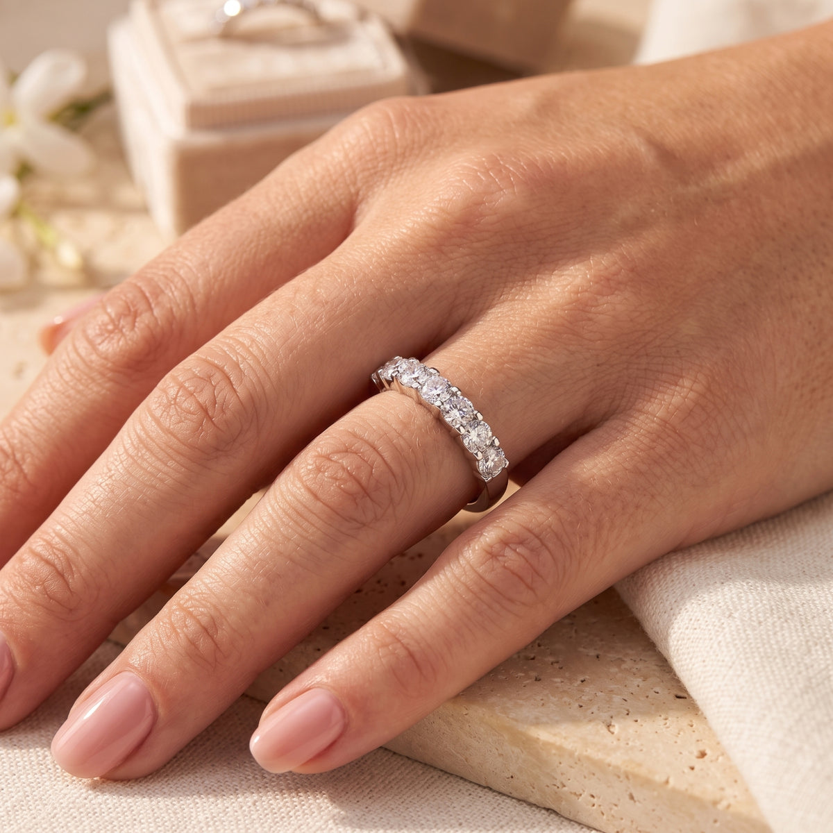 Seven-stone silver ring with round clear stones worn on a finger.