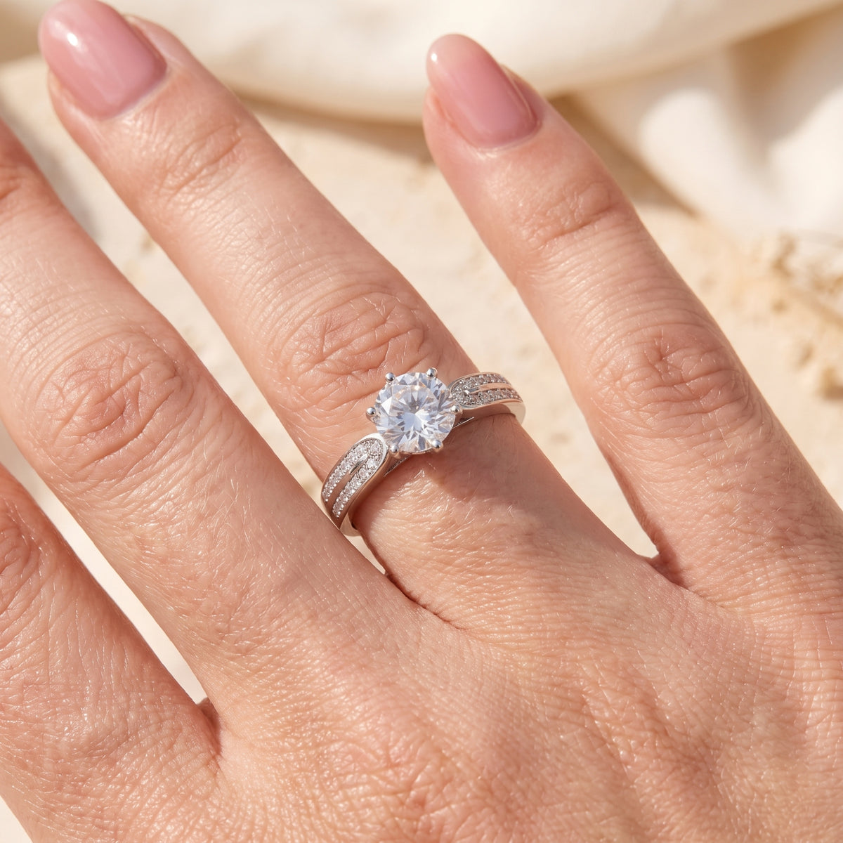 Silver split-shank ring worn on a finger, showing a round clear center stone and pave-set band accents.