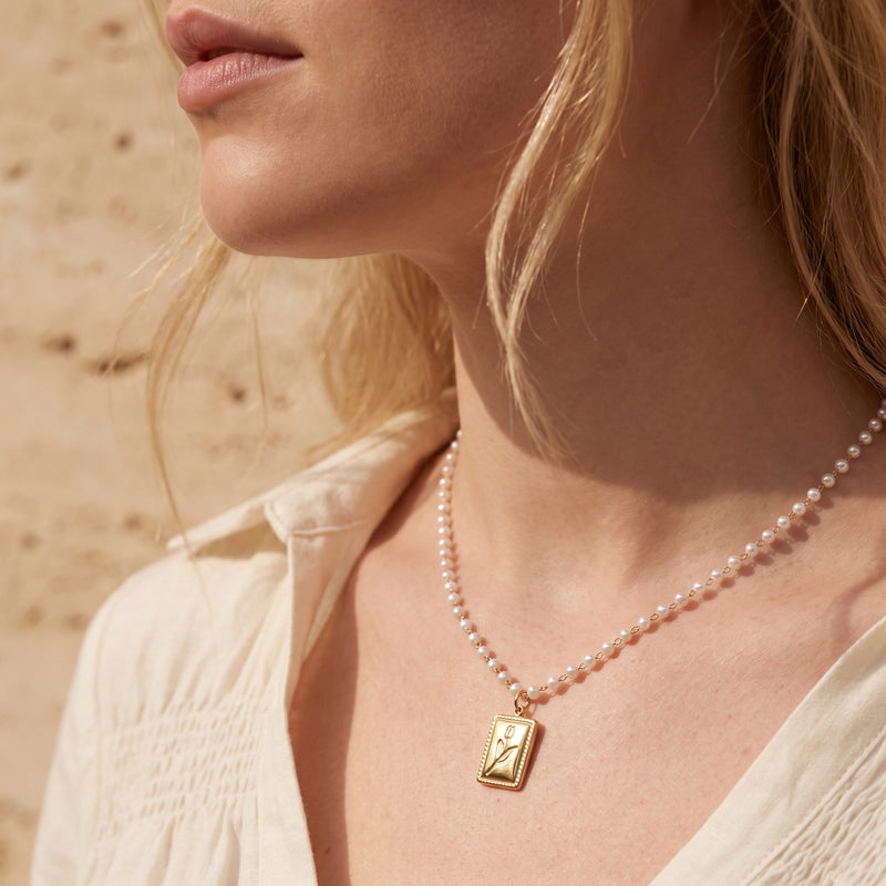 Model wearing the gold-tone rectangular tulip pendant necklace strung on a delicate white pearl beaded chain.