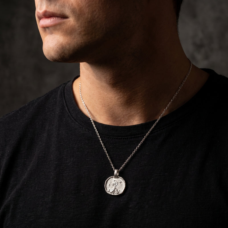 Man wearing the silver swallow medallion necklace over a black T-shirt, shown from the side.