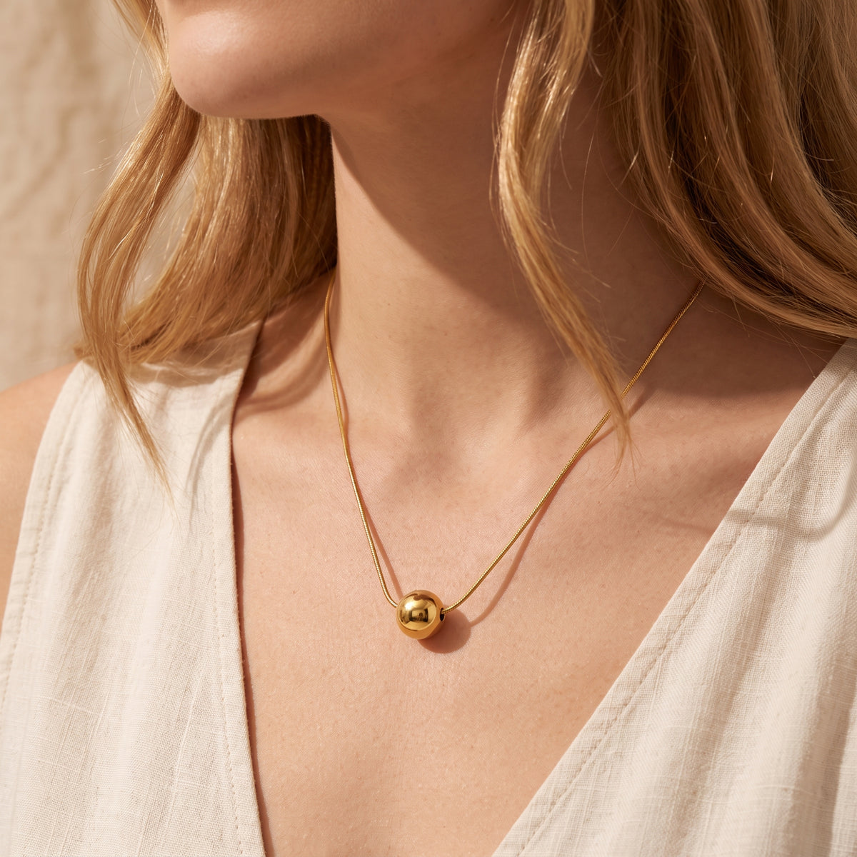 Close-up of a model wearing the gold-tone sphere necklace over a white V-neck top.