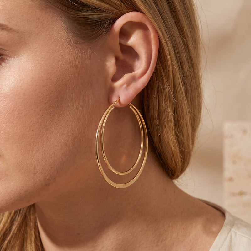 Close-up side view of a model wearing one gold-tone double hoop earring with two concentric circles.
