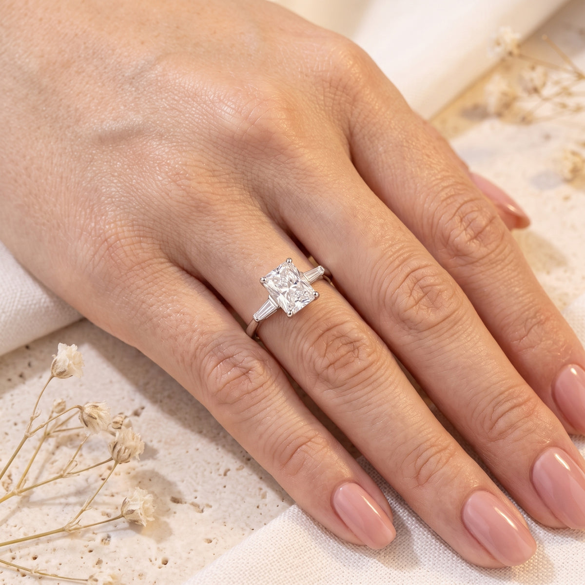 Silver three-stone ring with a radiant-cut center stone and tapered baguettes, shown worn on a hand.