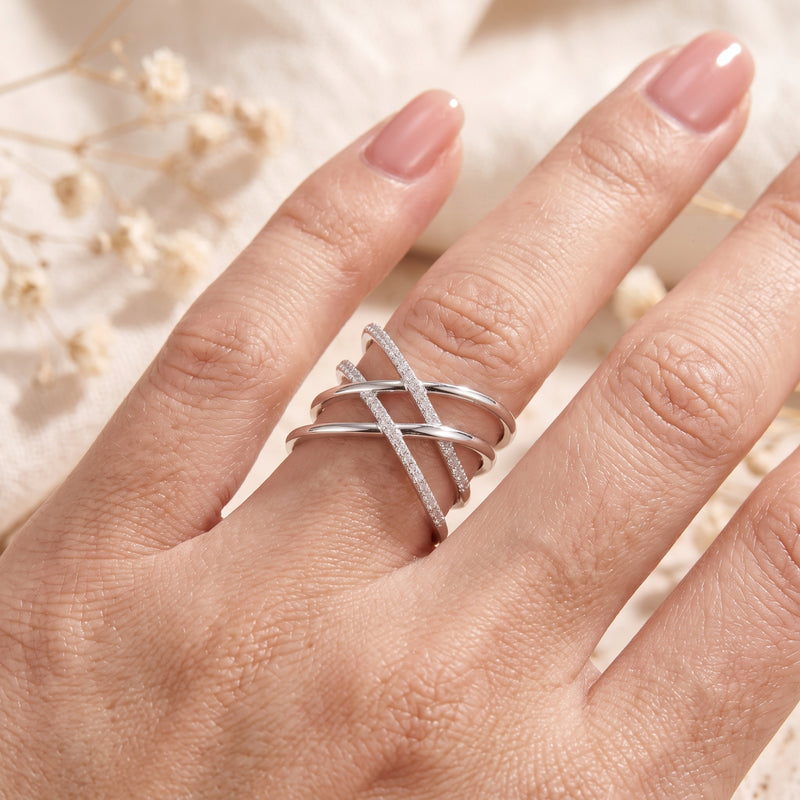 Close-up of a hand wearing a silver multi-band crossover ring with pavé stone accents.