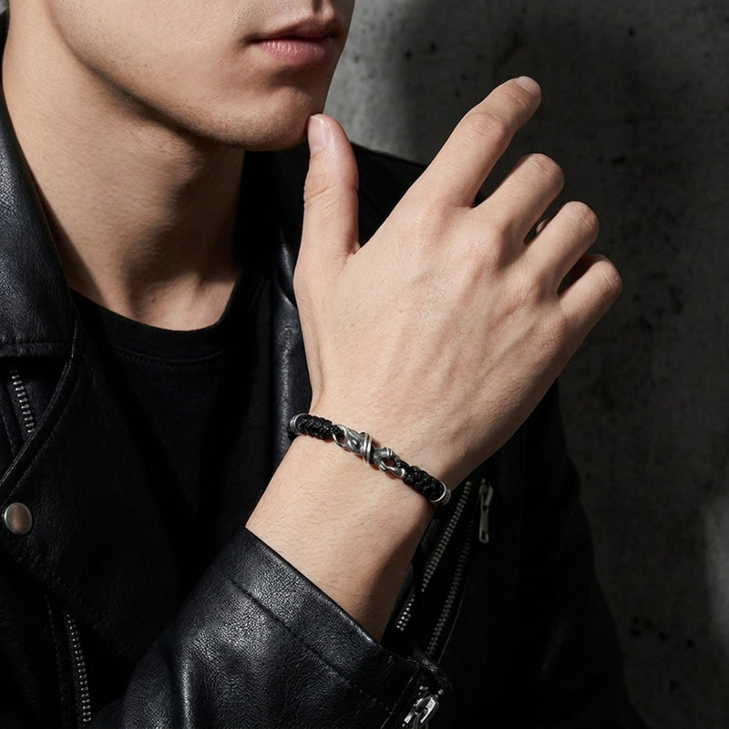 Model wearing the black woven cord bracelet with its branch-textured clasp visible, paired with a black leather jacket.