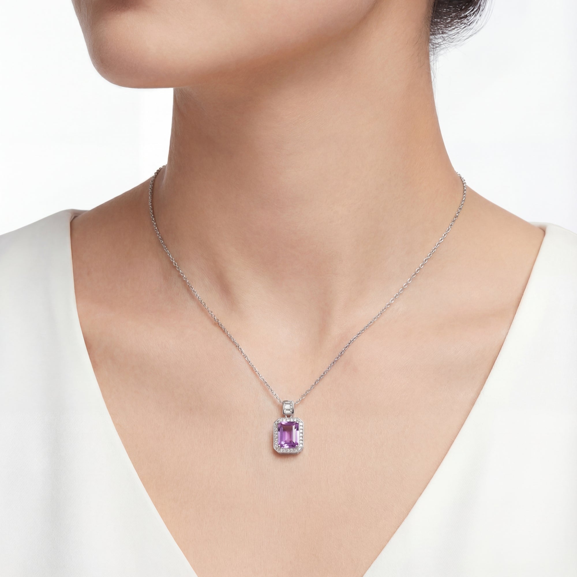Front view of a model wearing a sterling silver necklace featuring a purple emerald cut simulated amethyst pendant.