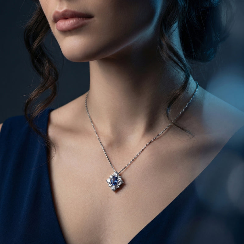 Model wearing the Miriel oval tanzanite halo necklace in white gold against a dark blue dress.
