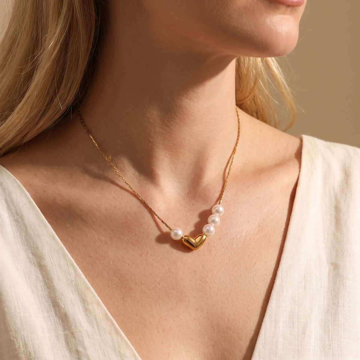 Model wearing the gold-tone asymmetrical pearl heart necklace with a cream V-neck top.