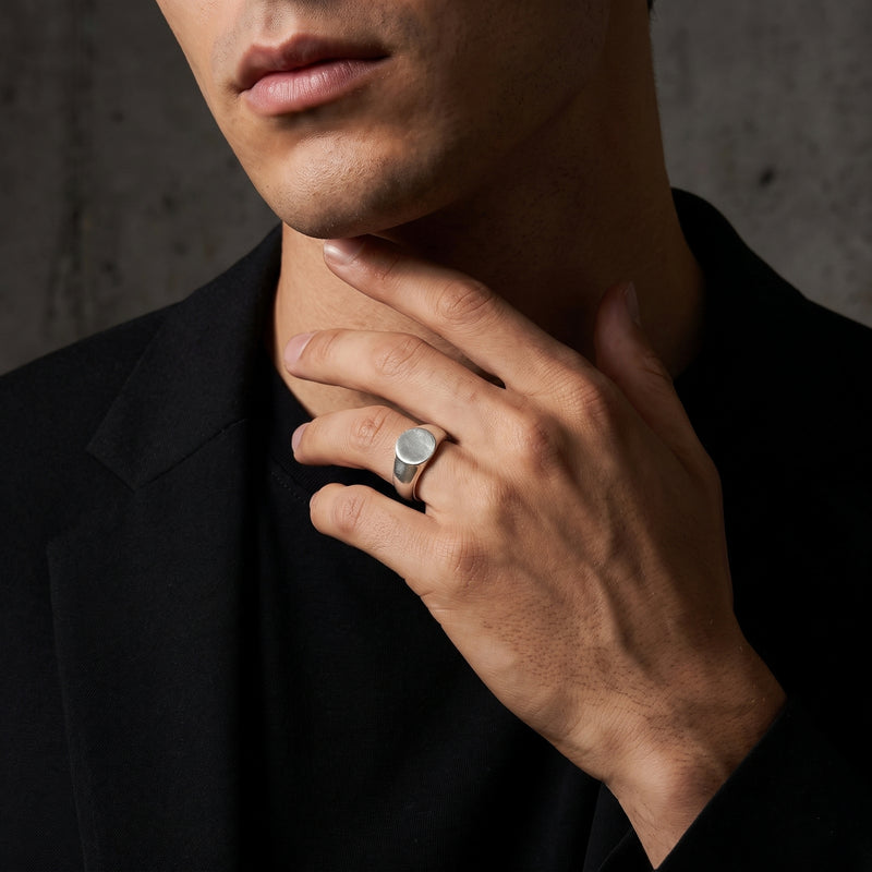 Model wearing the silver ring on a ring finger, with a hand raised near the neck against a dark backdrop.