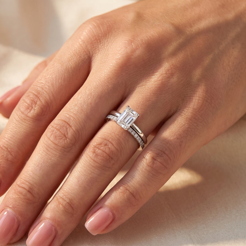 Close-up of a hand wearing the silver emerald-cut ring stacked with a clear pavé accent band.