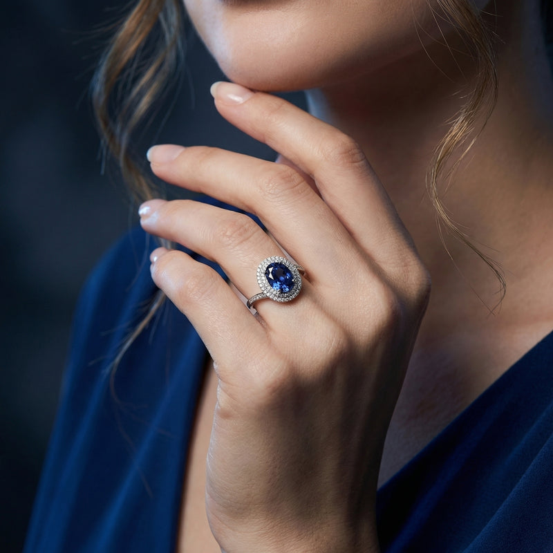Sterling silver oval tanzanite double halo ring worn on a woman's hand against a dark blue background.