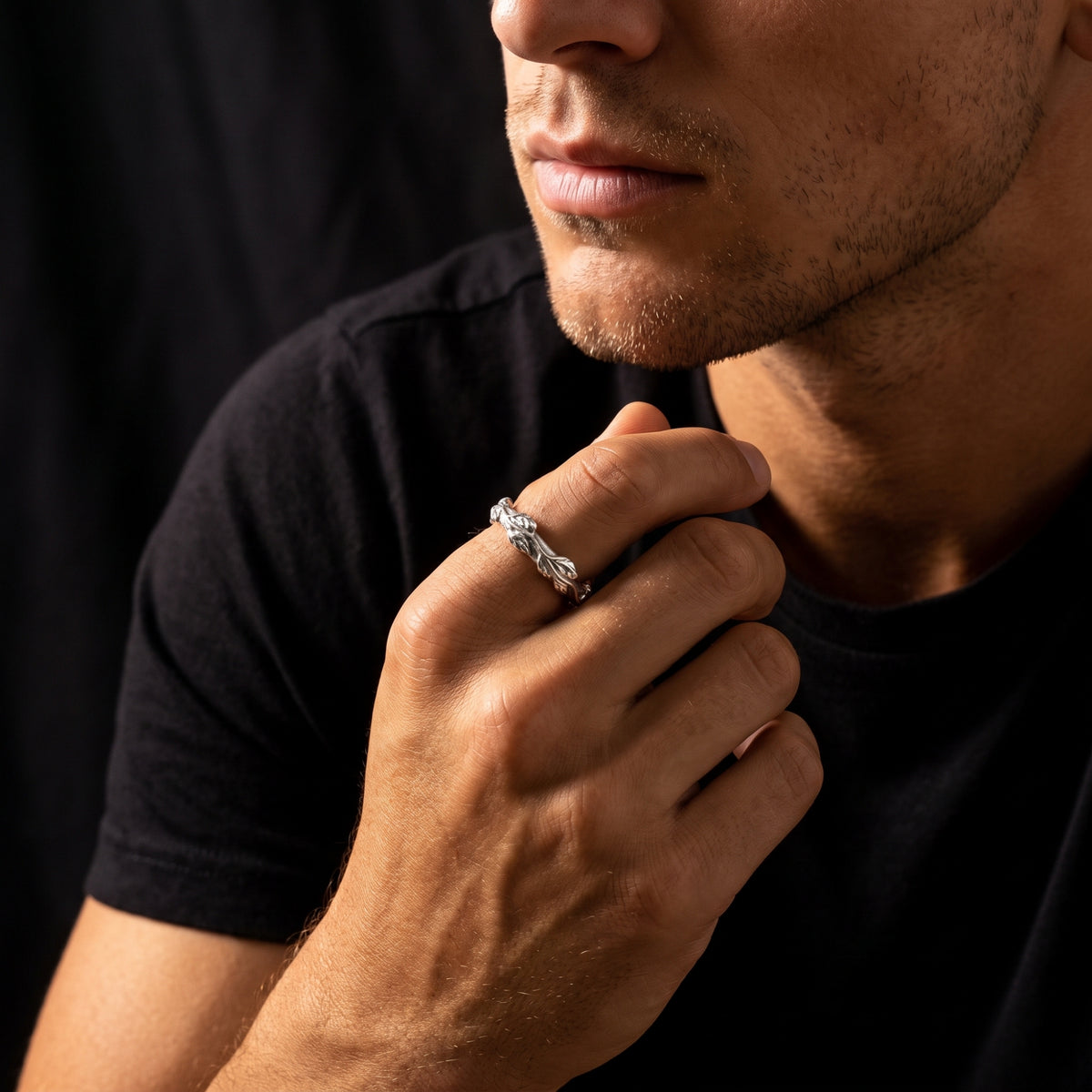 Man wearing the silver leaf-patterned open ring on his index finger, hand resting under his chin.