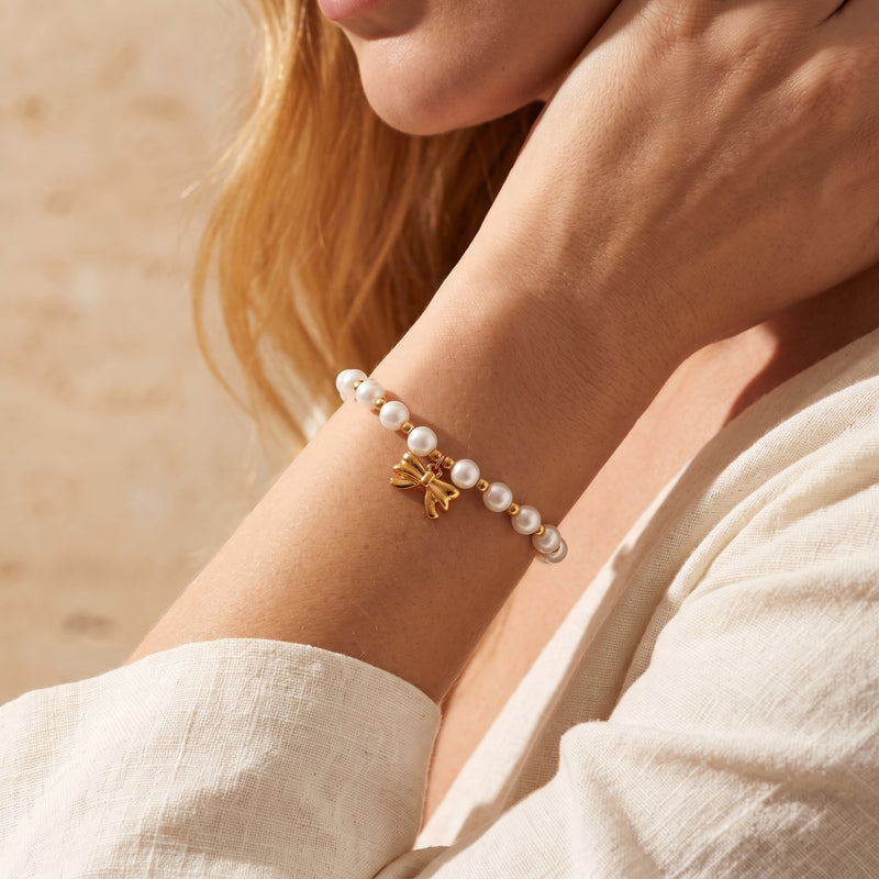 Close-up of a woman wearing the pearl bracelet with a gold-tone bow charm on her wrist.