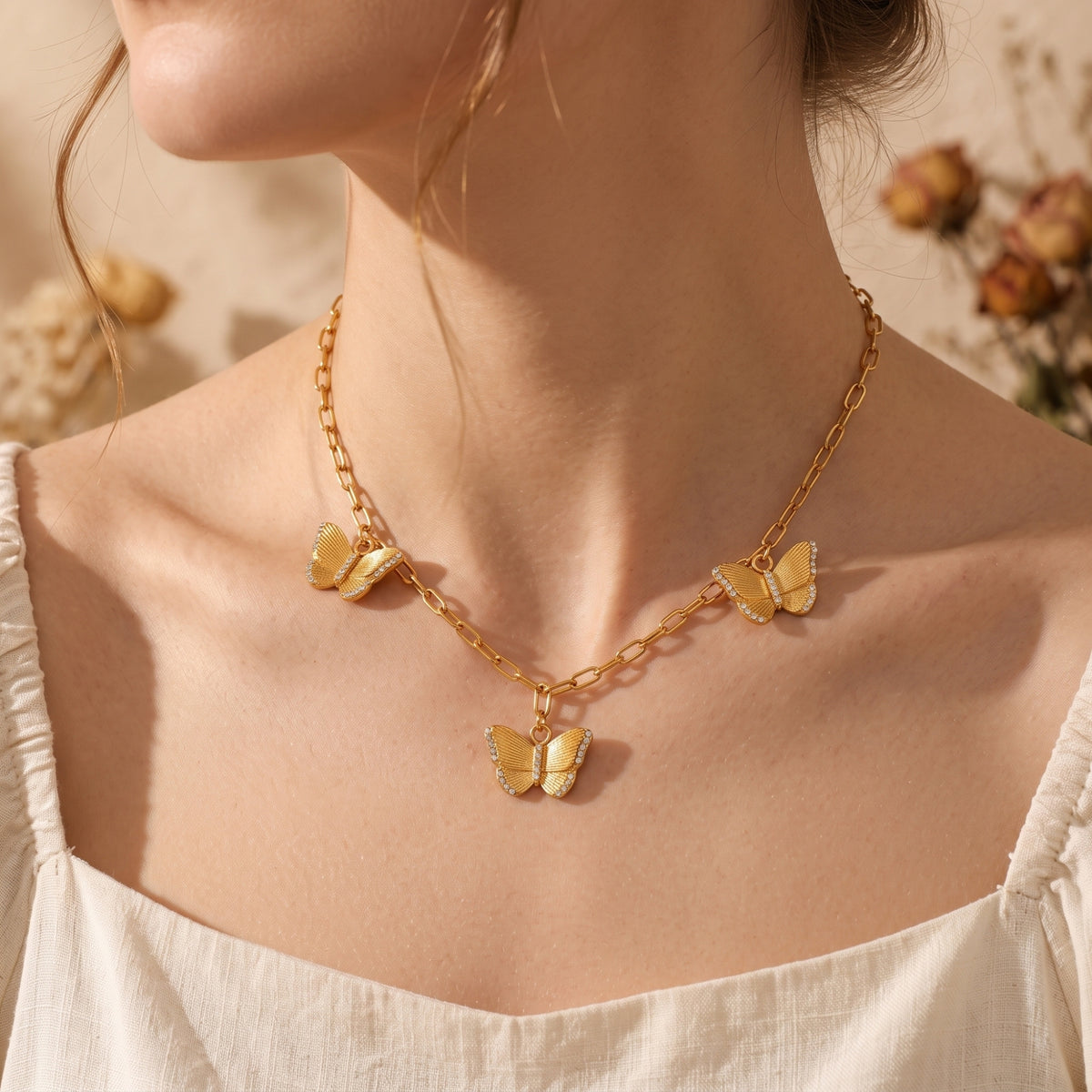Model wearing the gold-tone paperclip necklace featuring three cz-accented butterfly charms.