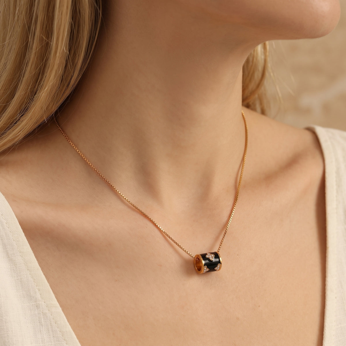 Side-view model wearing a gold-tone necklace with a black enamel barrel pendant resting near the collarbone.