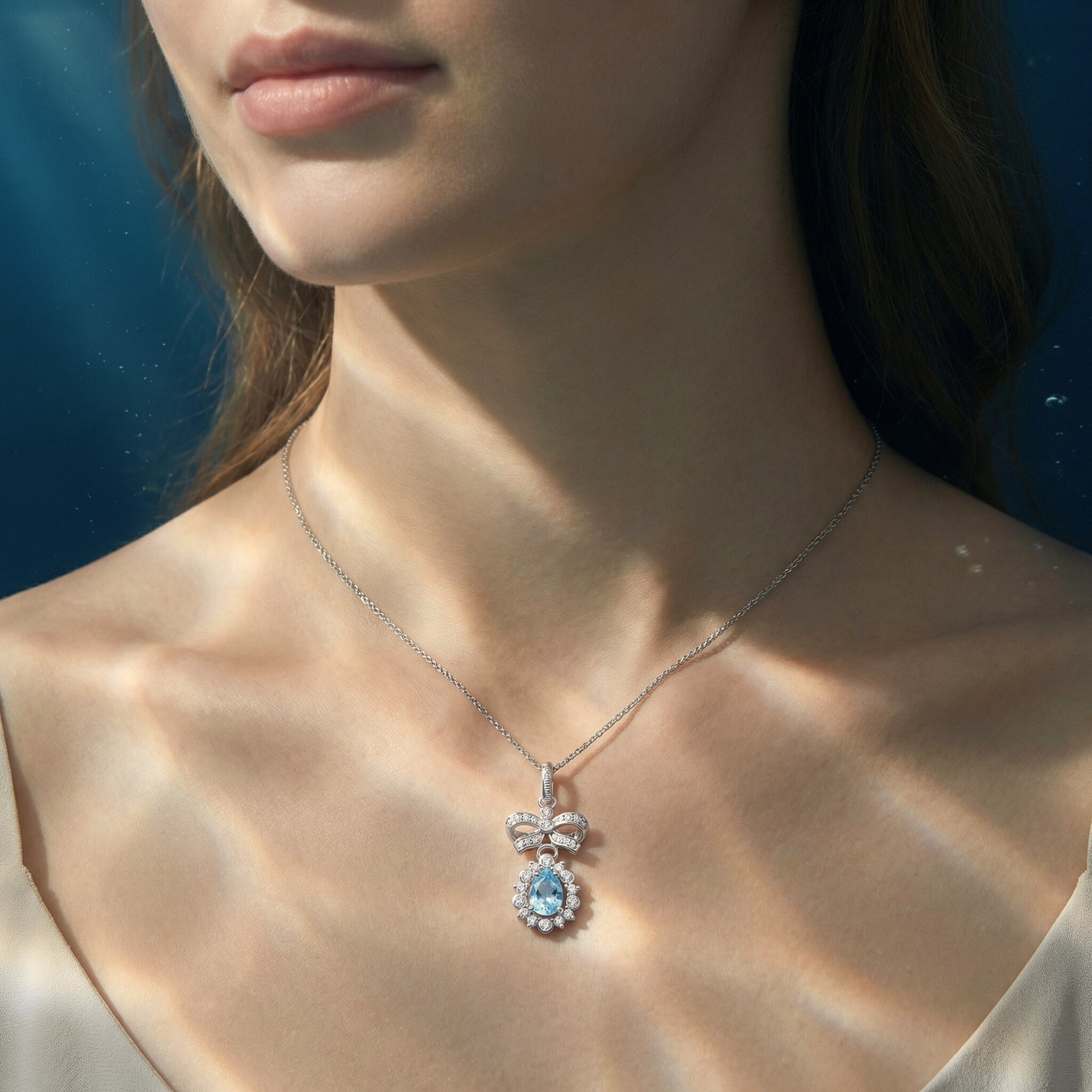 A woman wearing the silver pear cut aquamarine pendant necklace with a diamond-accented bow on a delicate chain.