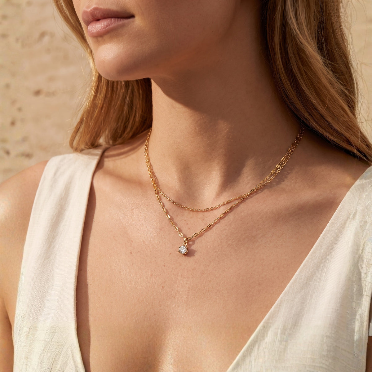 On-model view of the layered gold-tone necklace with a round solitaire pendant against a V-neck top.