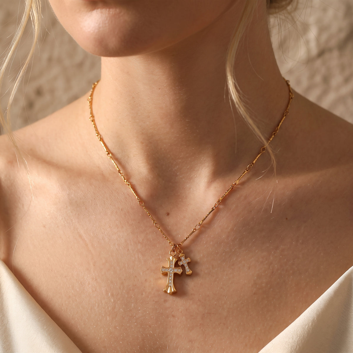 Gold-tone double cross pendant necklace worn at the base of a model's neck.