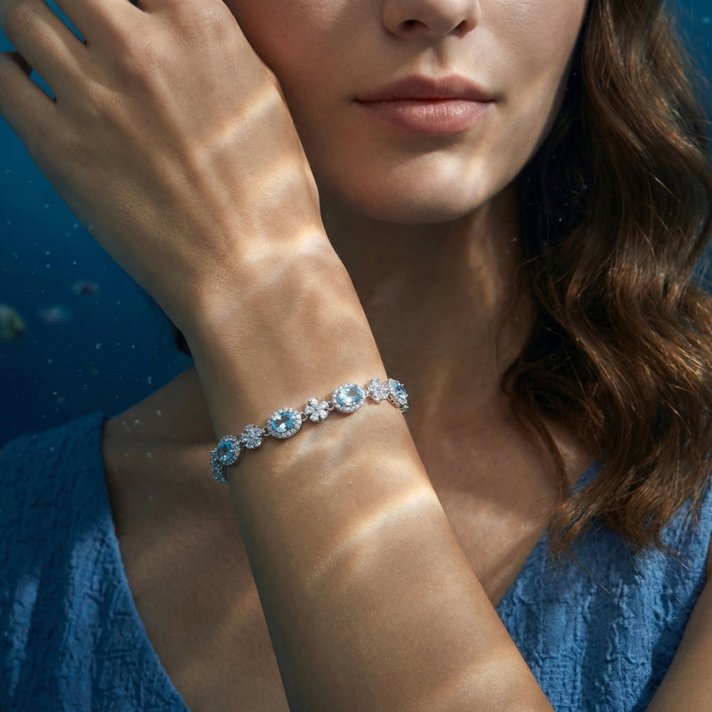 Women's white gold bracelet with oval aquamarine stones and flower accents worn on a model's wrist.