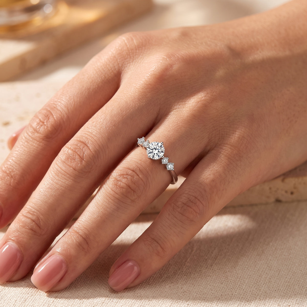 Silver solitaire ring with a round center stone and accent side stones worn on a person's hand.