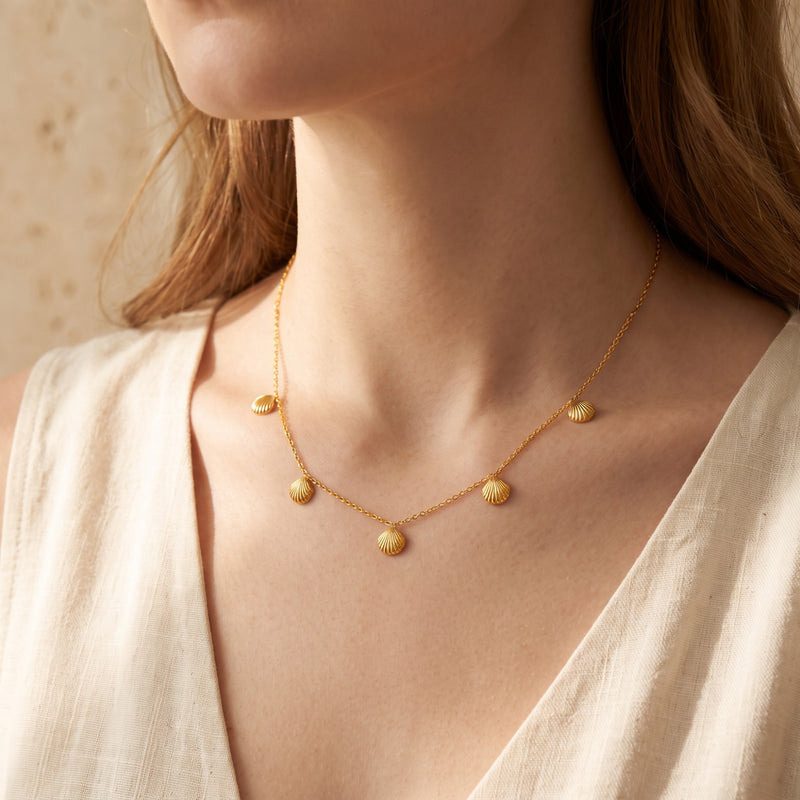 Front view of a model wearing the gold-tone scallop shell station necklace with a cream sleeveless top.