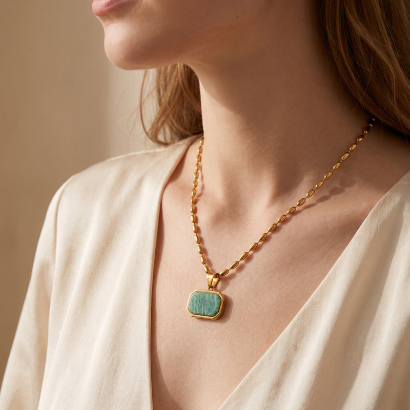 Model wearing a gold-tone bead chain necklace with an octagonal green Amazonite pendant over a V-neck top.