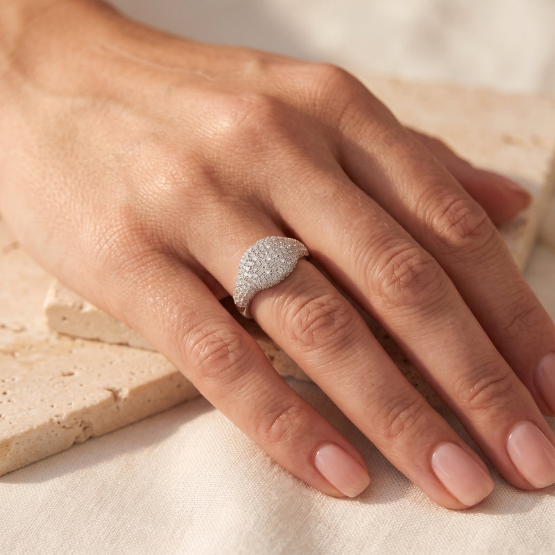 Overhead view of a solid gold pave dome ring in white gold with clear simulated diamonds worn on a ring finger.