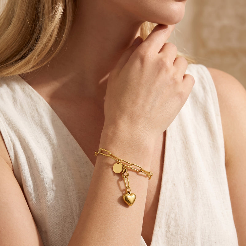 Model wearing the gold-tone link bracelet with dangling heart and round disc charms on her wrist.