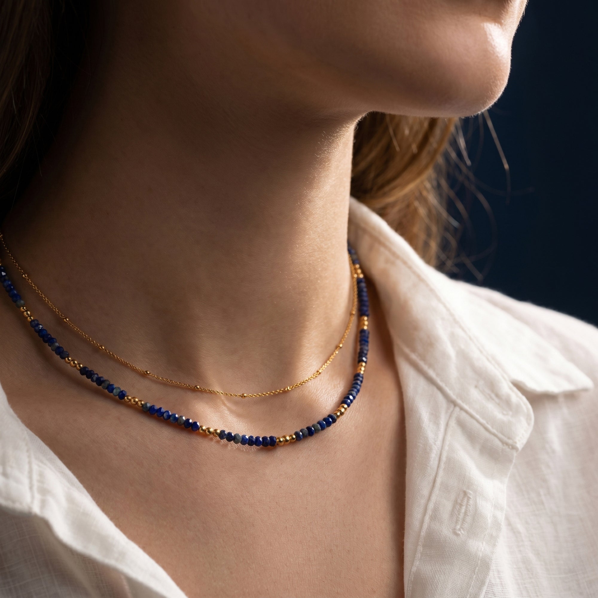 Woman wearing the Azure Skies layered gold necklace with faceted lapis lazuli beads and a thin gold chain.
