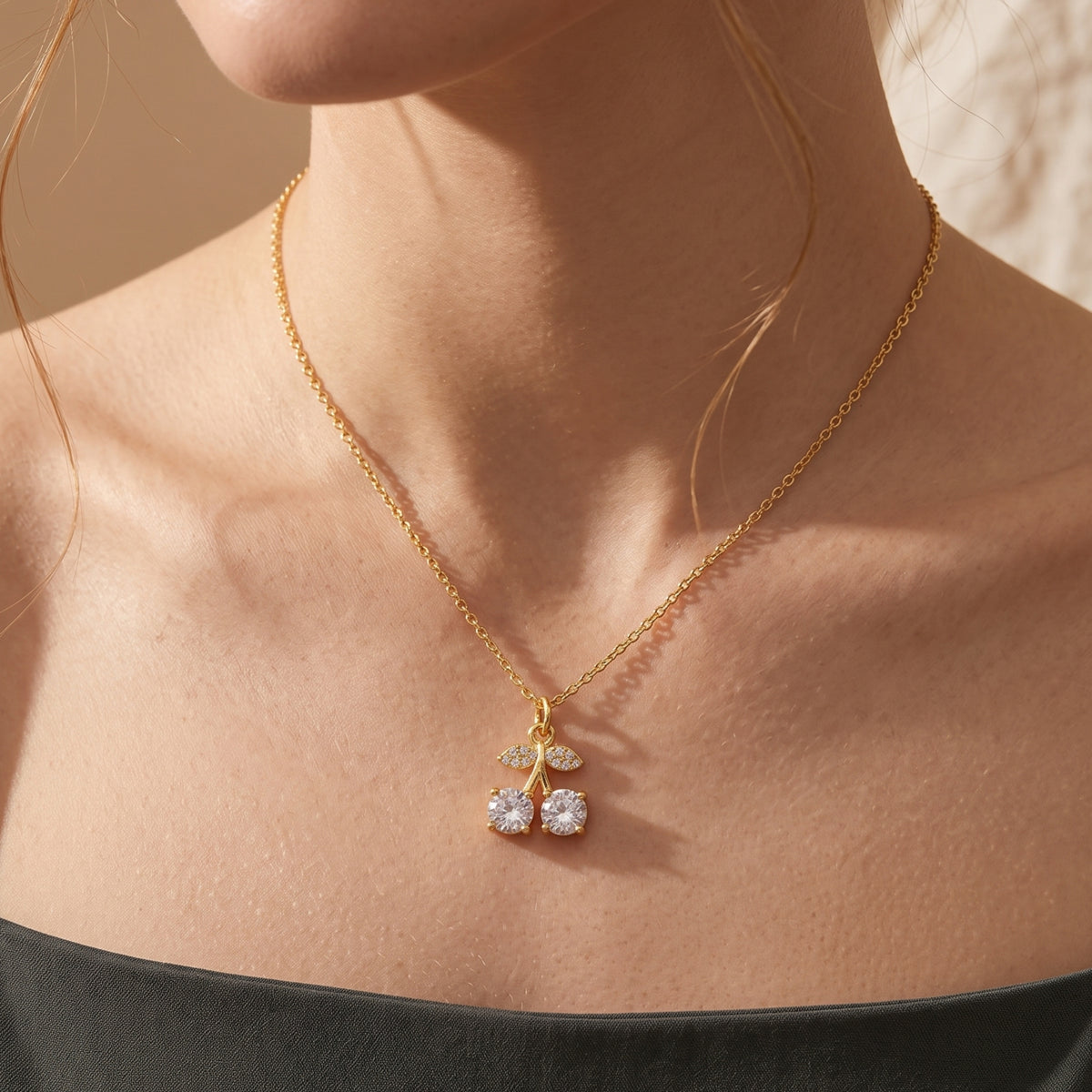 Gold-tone crystal cherry pendant necklace worn against the collarbone with a black off-shoulder top.
