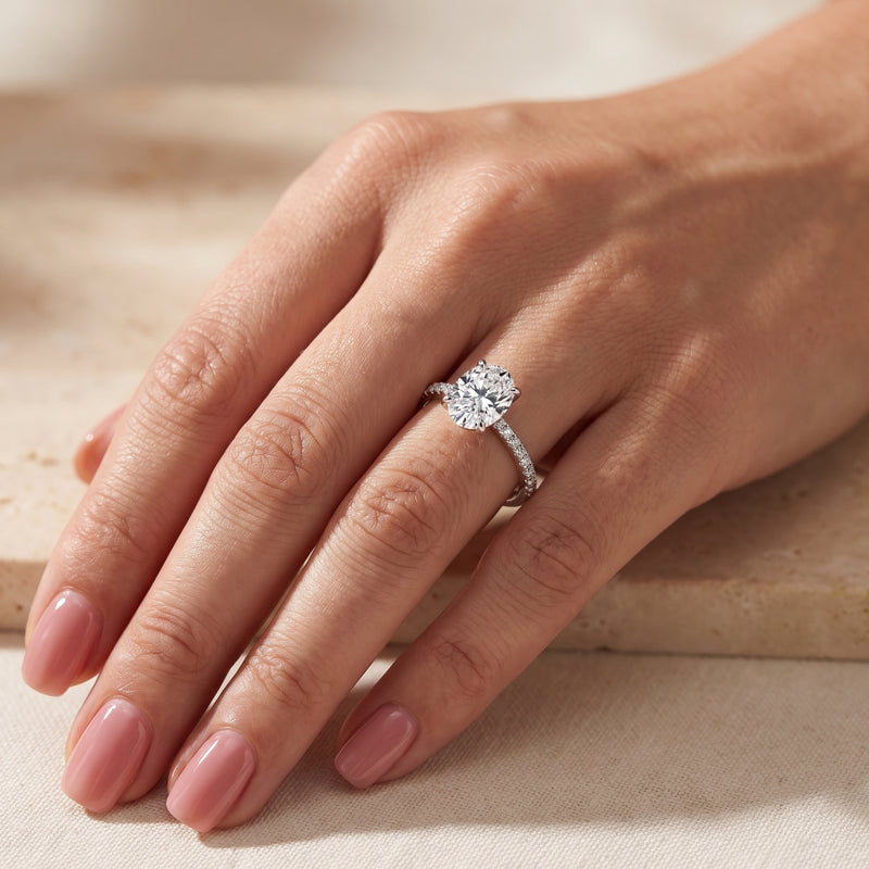 Silver ring with a clear center stone and pavé band worn on a ring finger, shown from an angled hand perspective.