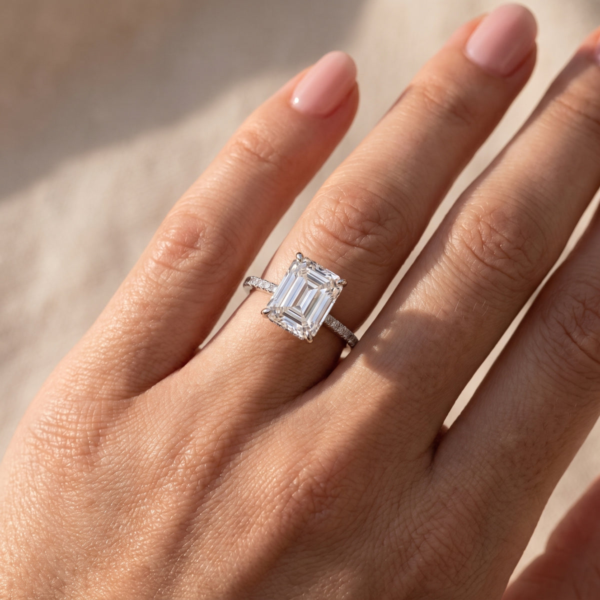 Close-up of the silver ring with an emerald-cut clear stone and pavé band worn on a finger.