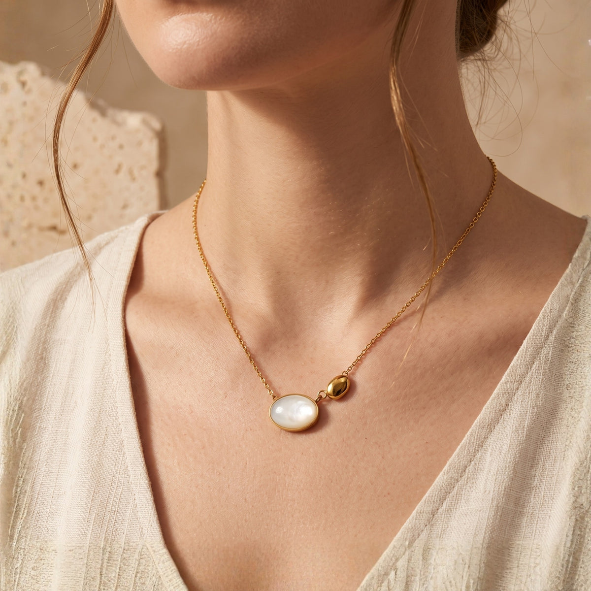 Model wearing a gold-tone necklace with an asymmetric mother-of-pearl oval and gold-tone pebble pendant.