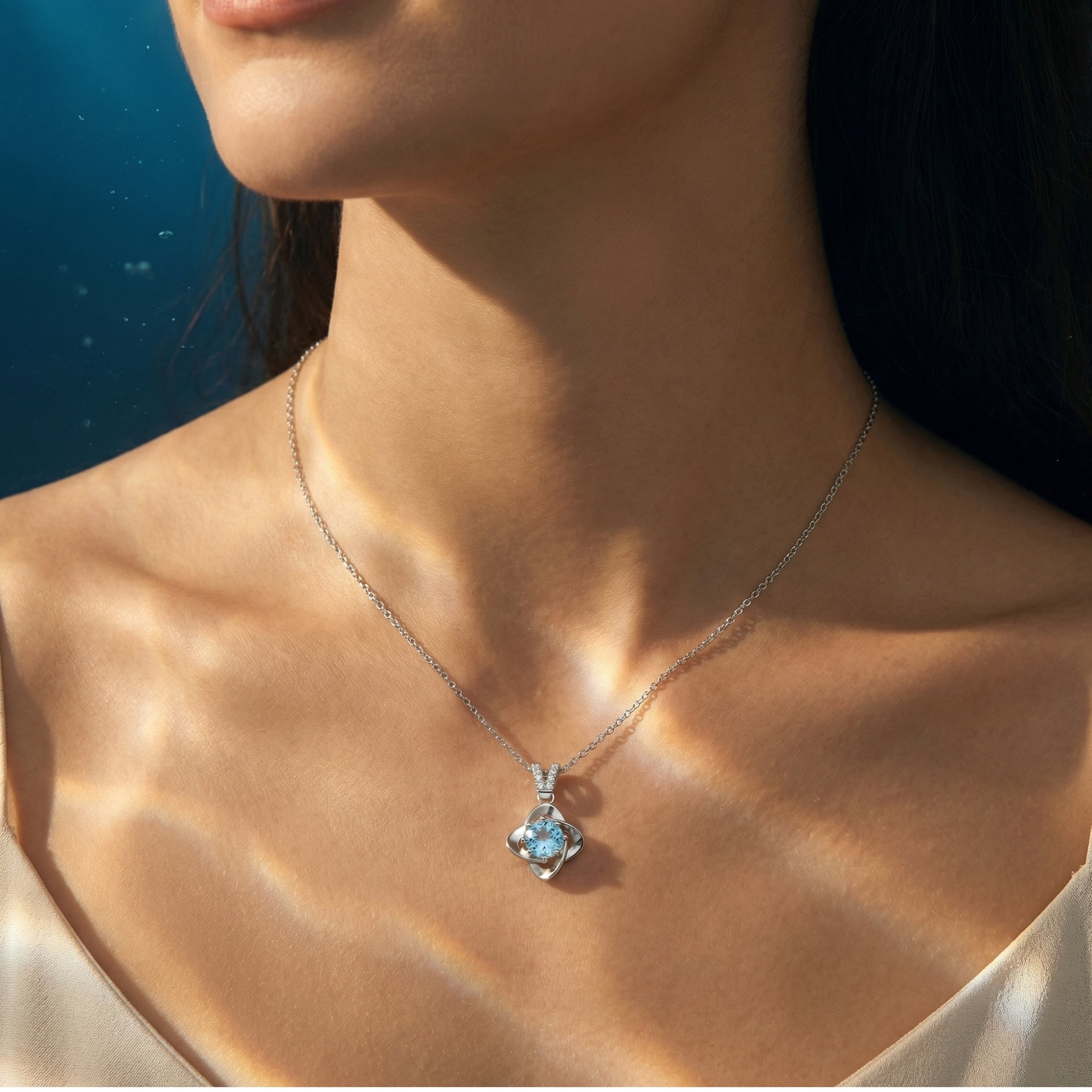 Model wearing the Alaina platinum necklace featuring a round cut aquamarine pendant against a sunlit background.