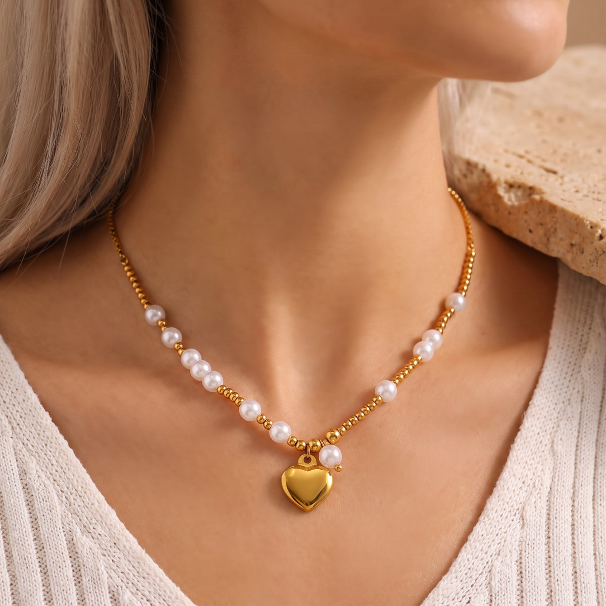 Front view of a model wearing a gold-tone beaded necklace with white pearls and a heart pendant.