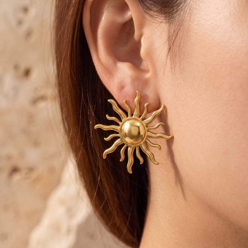 Close-up side view of a gold-tone sunburst stud earring worn on an earlobe.
