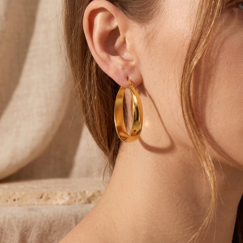 Model wearing one gold-tone tapered hoop earring in a close-up side profile.