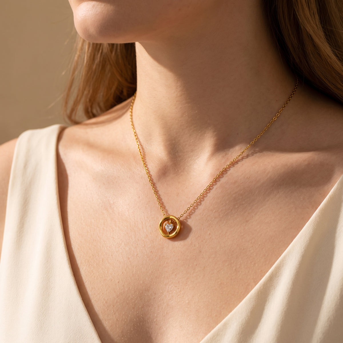 Angled close-up of a model wearing the gold-tone heart pendant necklace over a cream V-neck top.