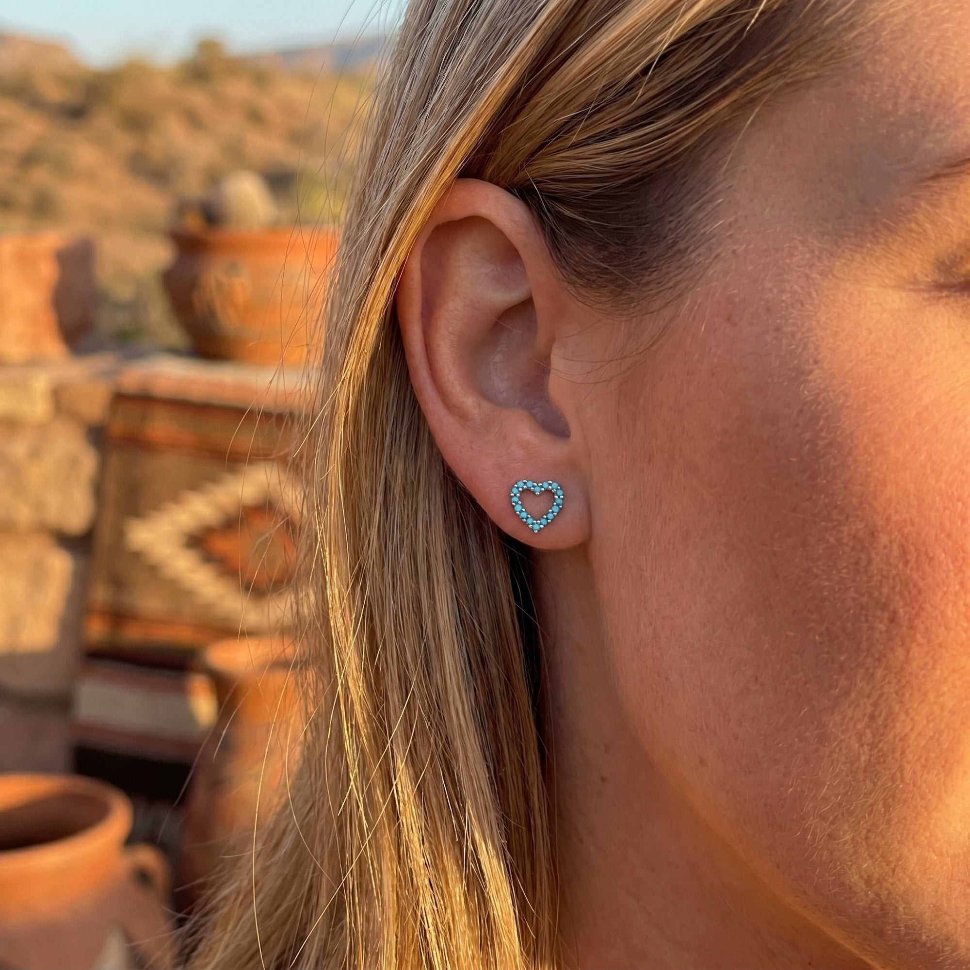 Woman wearing a silver heart-shaped turquoise stud earring outdoors against a desert background.