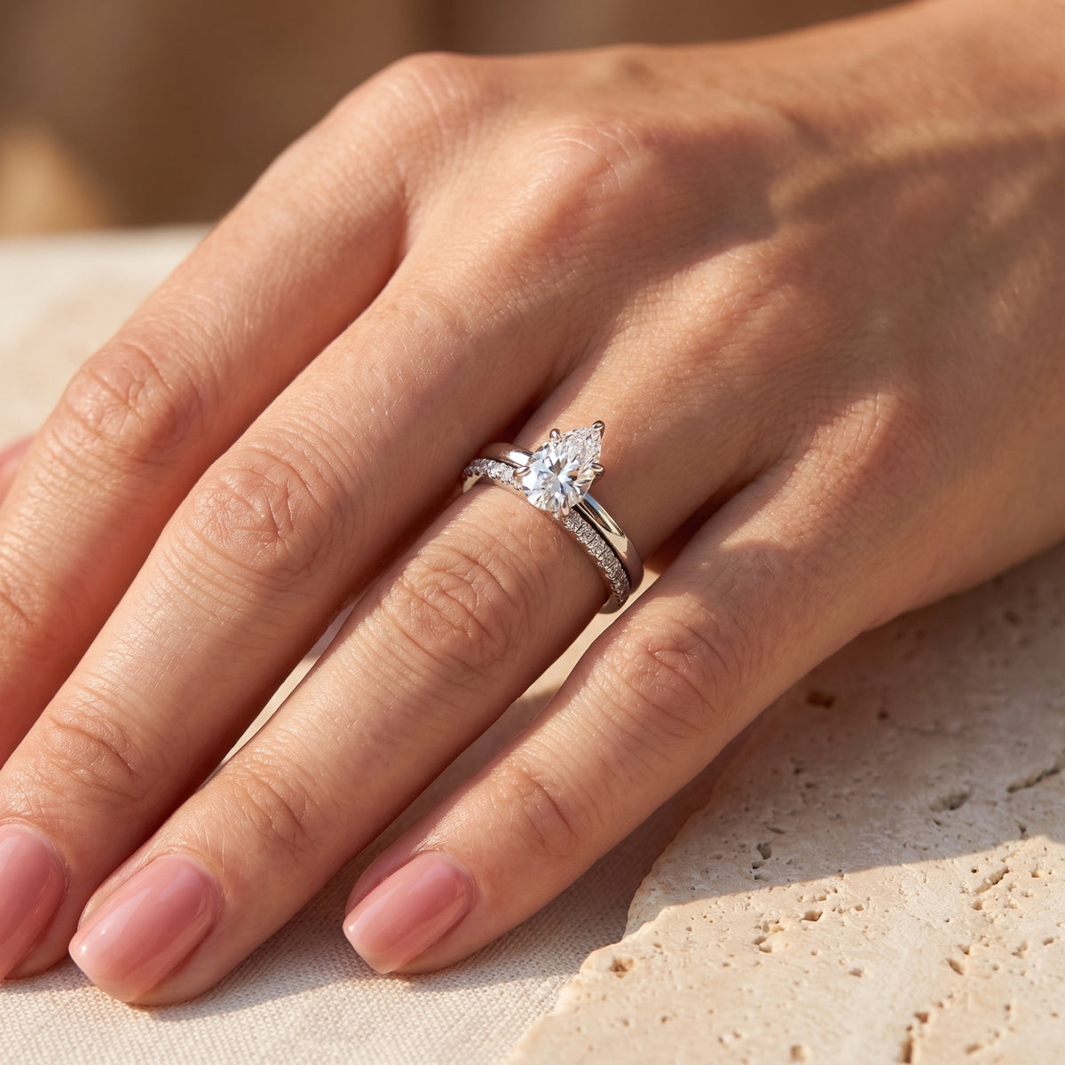 Angled close-up of a hand wearing the silver-toned pear-cut solitaire and pavé band as a stacked set.