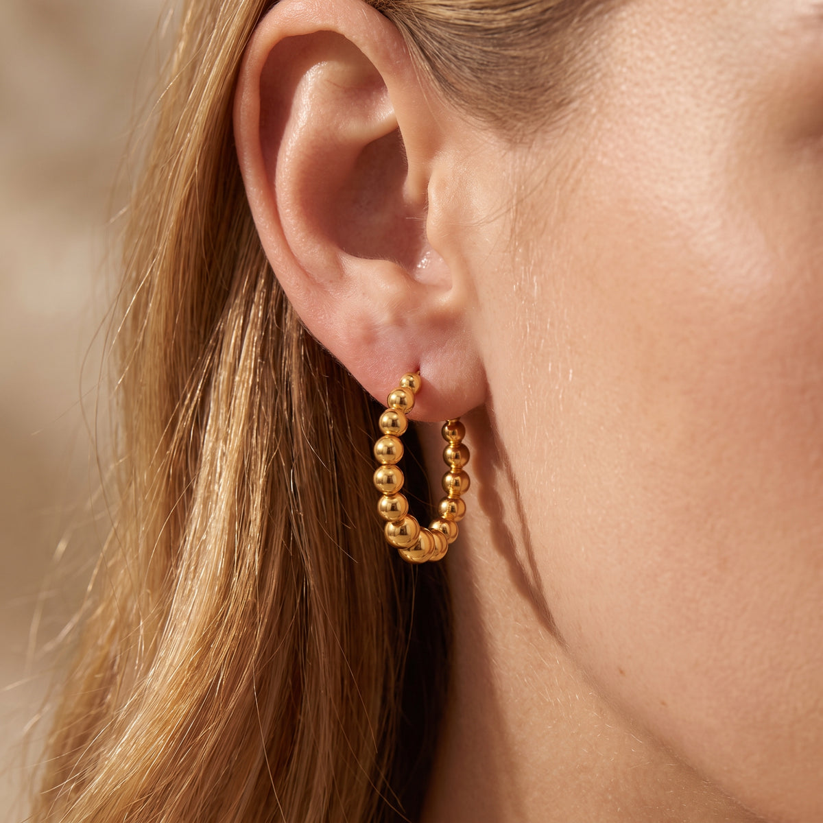 Close-up of a gold-colored graduated beaded hoop earring worn on an earlobe.