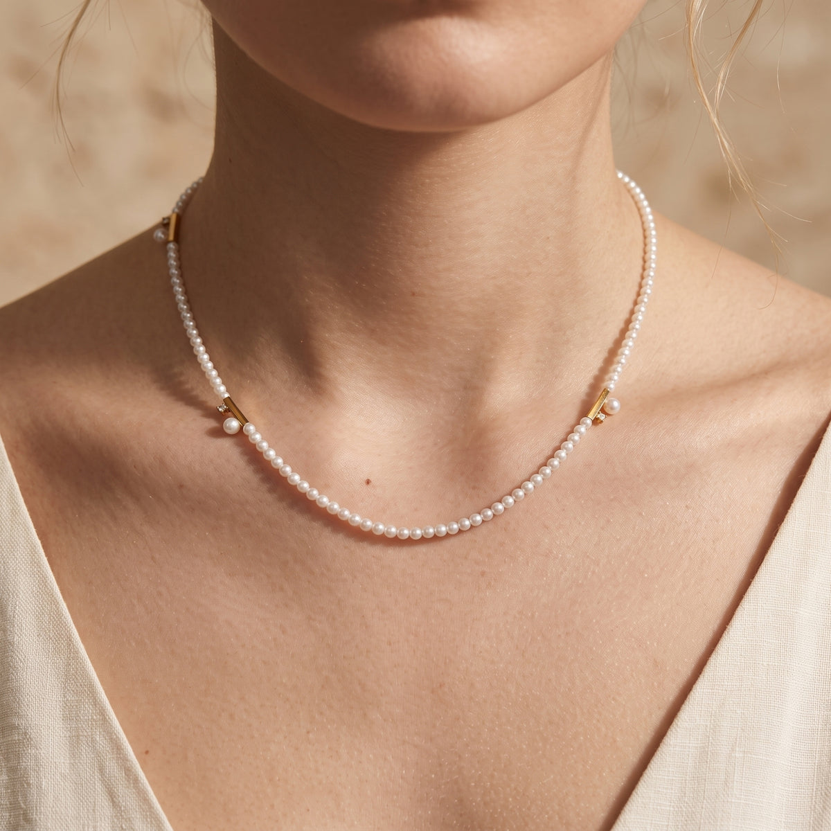Front close-up of a model wearing the gold-tone pearl bar station necklace over a cream V-neck top.