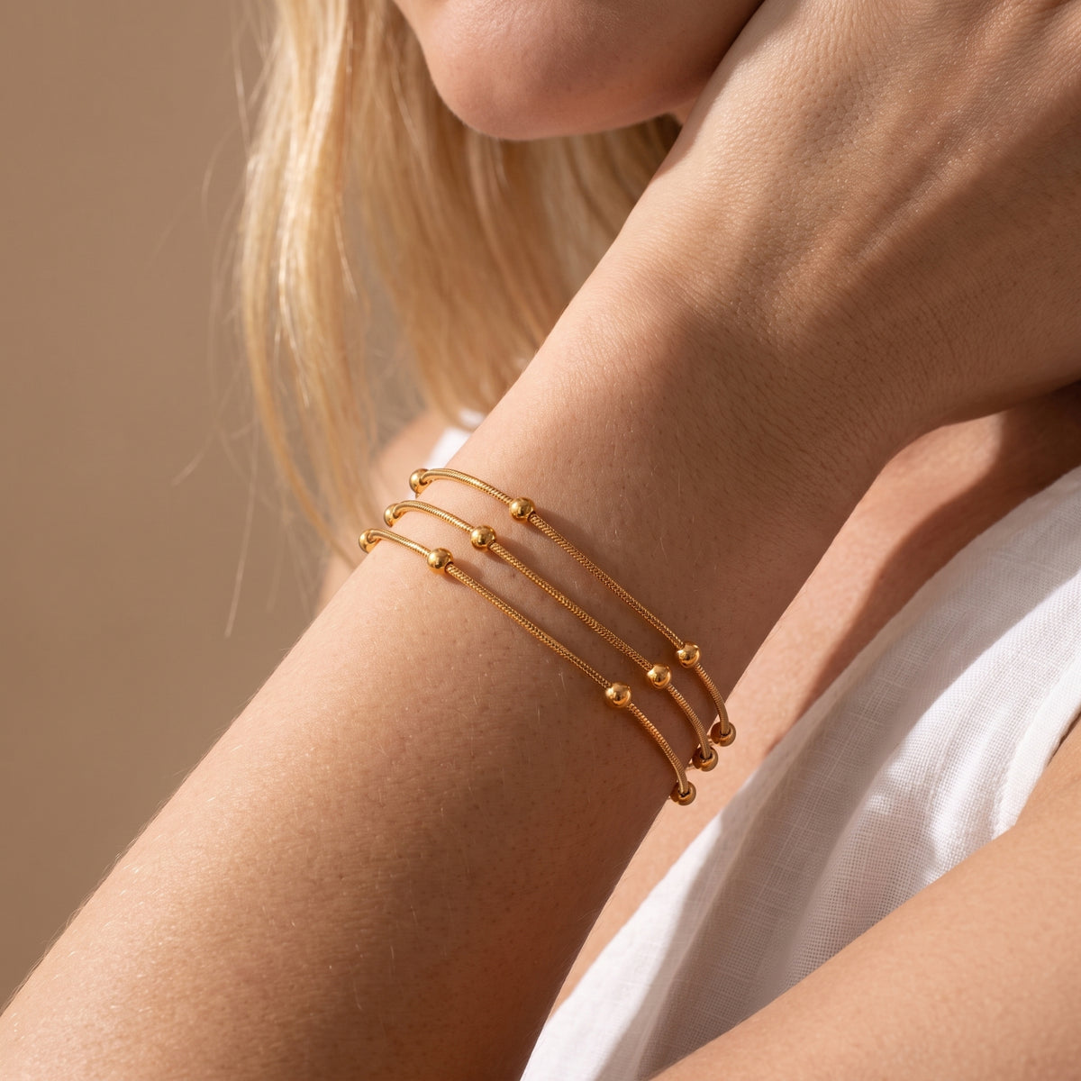 Model wearing the gold three-strand beaded snake chain bracelet around her wrist in warm light.