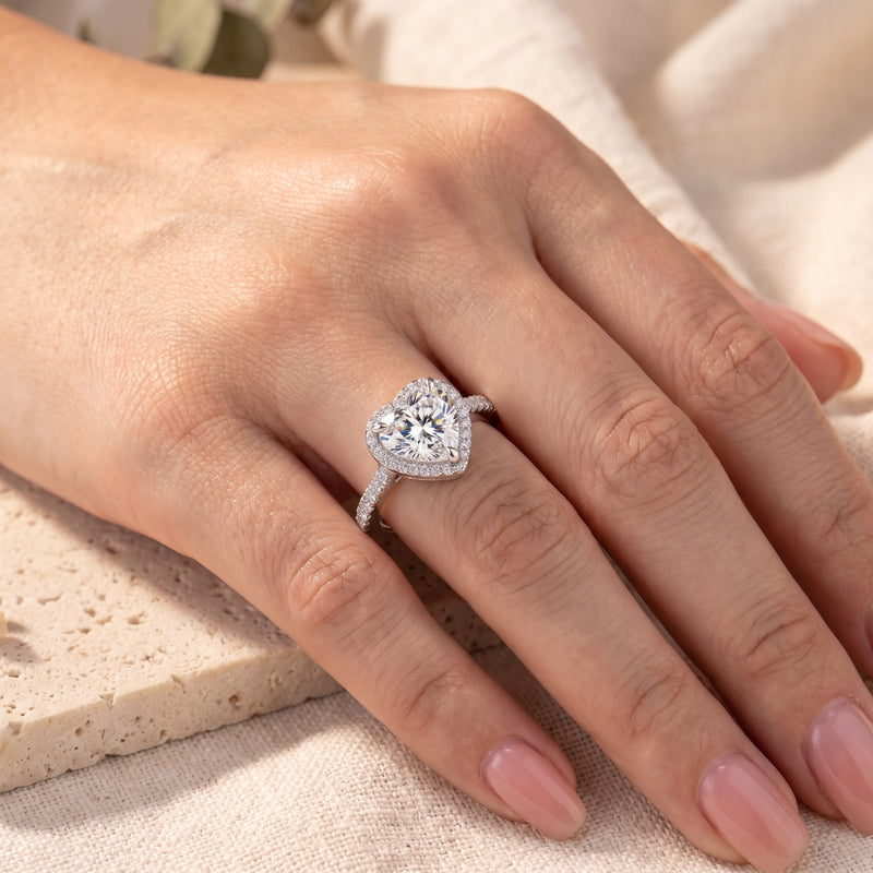 Angled view of a silver heart-shaped halo ring with a simulated diamond worn on a hand.