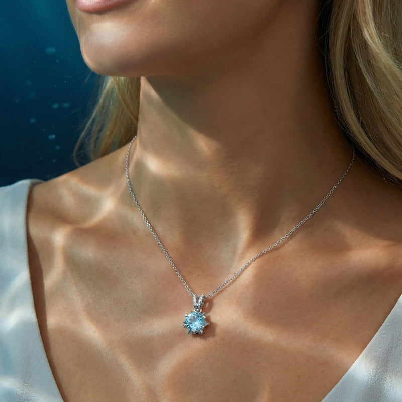 Woman wearing the Liriope platinum necklace with a round natural aquamarine pendant against a soft blue background.