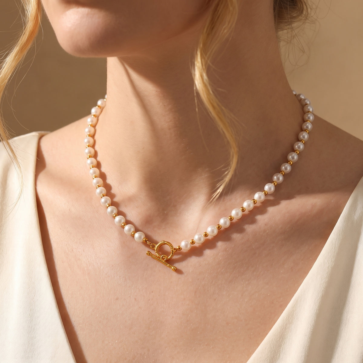 White simulated pearl necklace with gold-tone spacer beads worn on a model, with the toggle clasp centered below the neck.