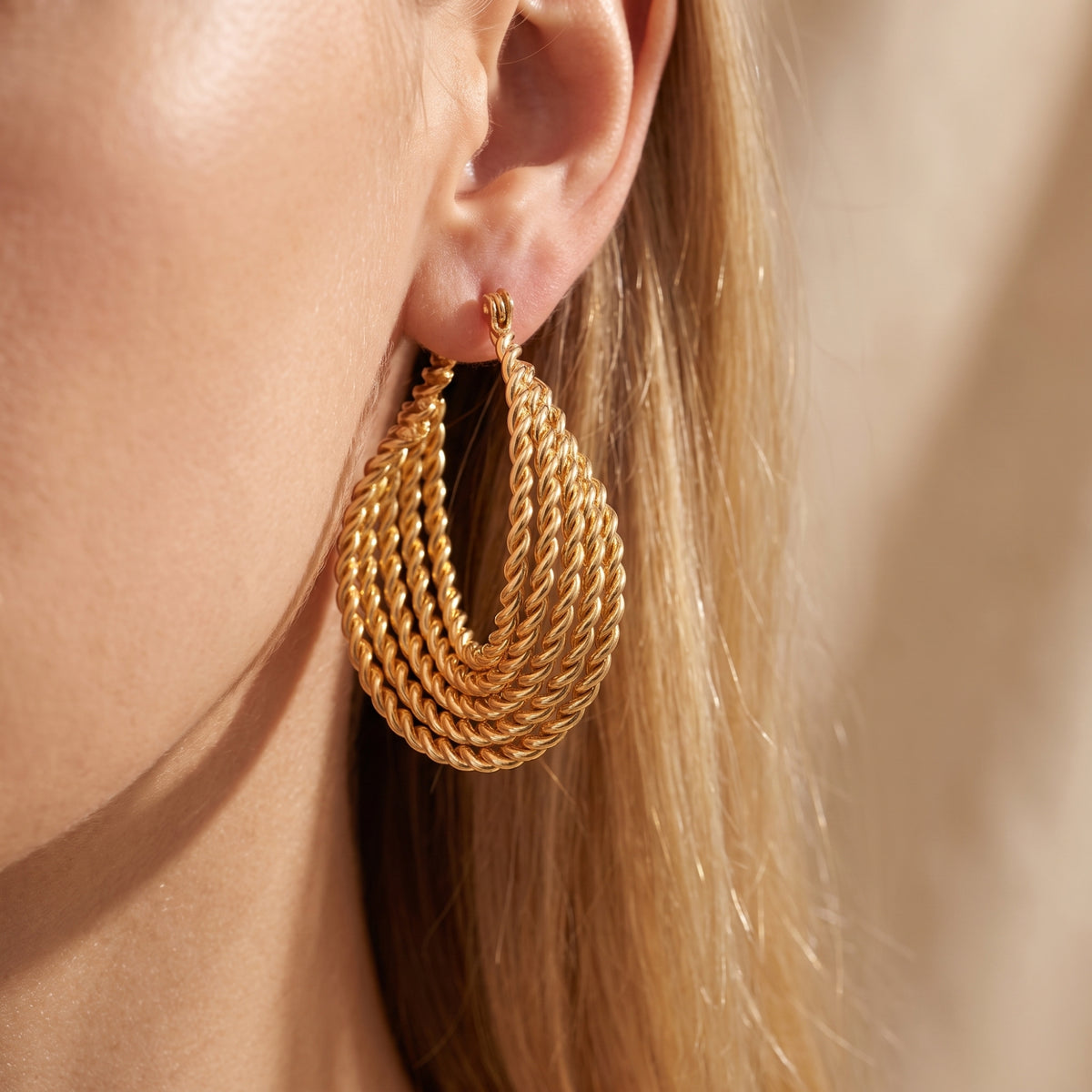 Side-profile close-up of a model wearing one gold-tone multi-strand twisted rope drop earring.