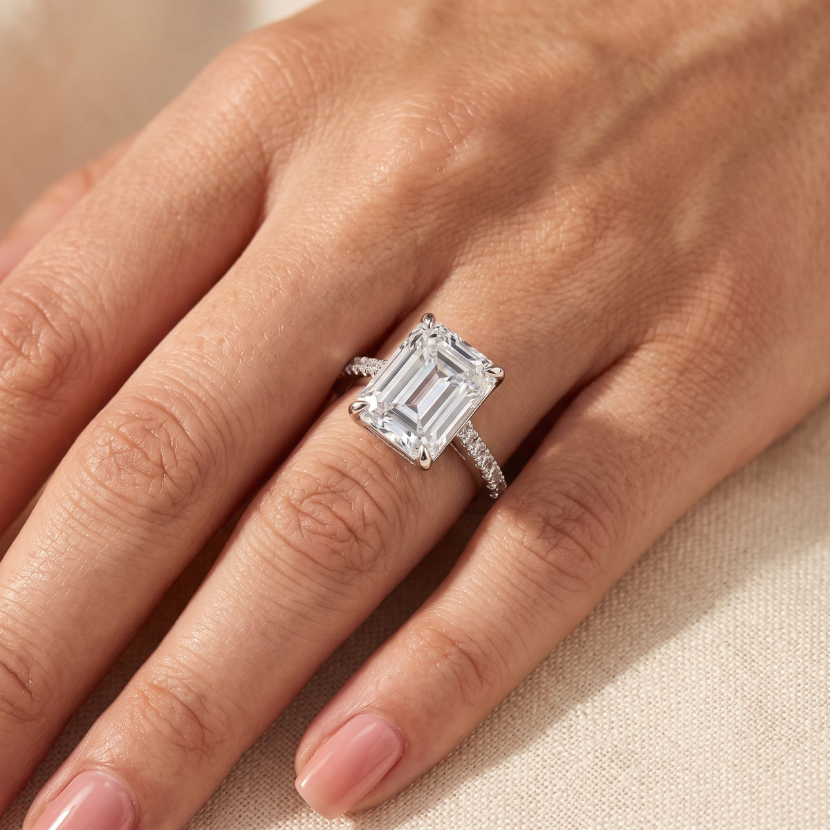 Emerald-cut solitaire ring with pave accent stones worn on a finger, viewed diagonally across the hand.